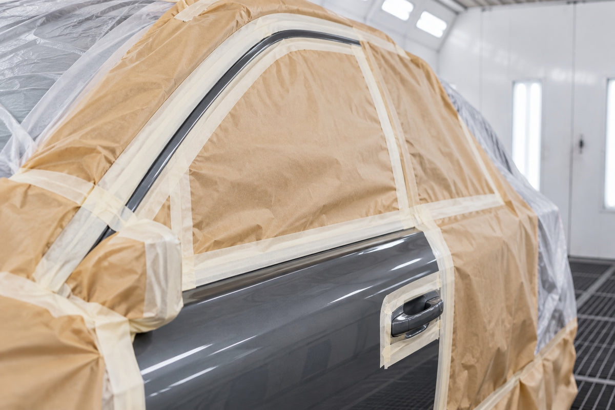 A car door masked with masking tape and paper in a spray booth, ready for painting